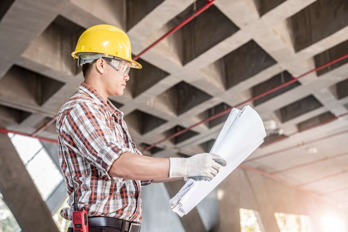 A worker in a hard hat reviews plans and permits for a building, commercial property management concept