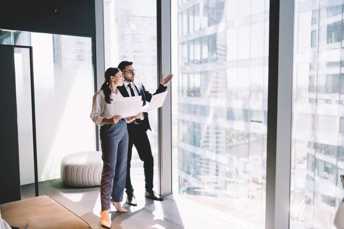 Two business people look out at an office building, commercial property management services concept